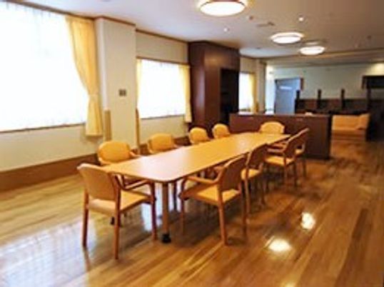 大きな木製のダイニングテーブルが中央に置かれた共有スペース。窓には黄色いカーテンが付けられている。