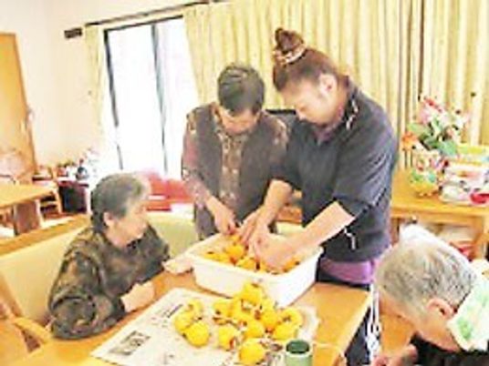 食堂のダイニングテーブルを囲んで干し柿作りをしている女性たちと若いスタッフ。皮をむかれた柿がたくさんある。