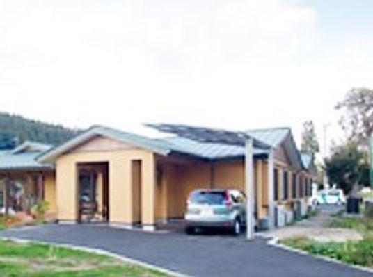 平屋建ての建物の玄関には車寄せがあり、シルバーの車が止められている。周辺には緑が多くある。