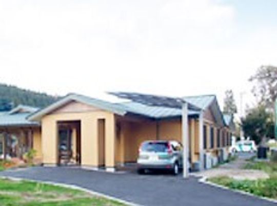 平屋建ての建物の玄関には車寄せがあり、シルバーの車が止められている。周辺には緑が多くある。