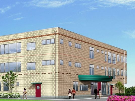３階建ての建物はベージュで車寄せが付き、周辺を木や花に囲まれている。