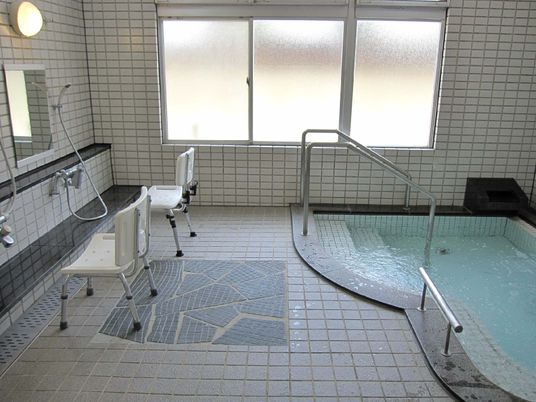 手すり付きの階段が付いた広い浴槽が設置された大浴場には、シャワーがあり、シャワーチェアも置かれている。