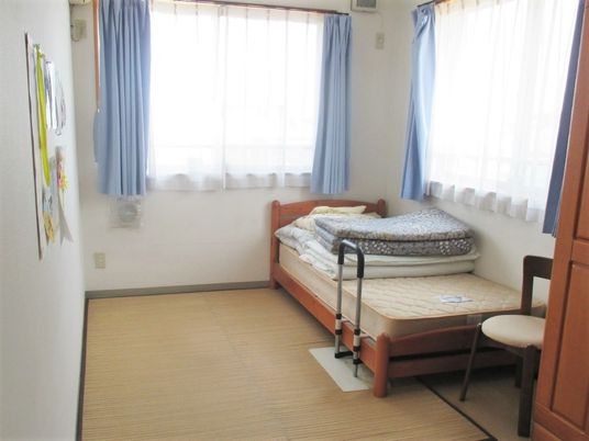 大きな窓が二つ付いた居室にはクローゼットやベッド、いすも置かれている。