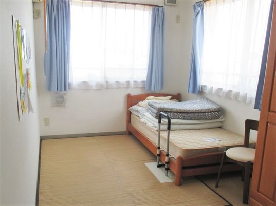大きな窓が二つ付いた居室にはクローゼットやベッド、いすも置かれている。