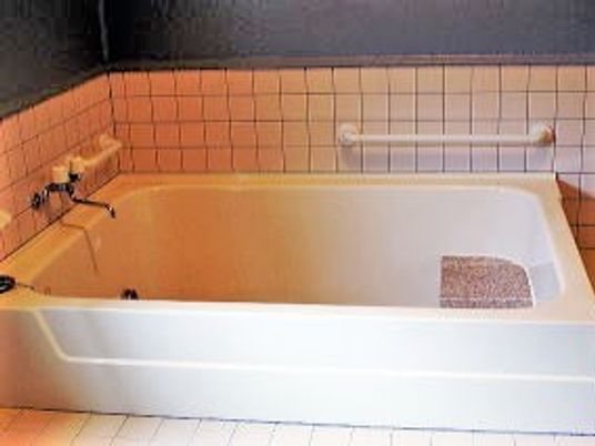 家庭用サイズの浴槽に手すりが付いている様子。タイル張りの壁と床が写っている