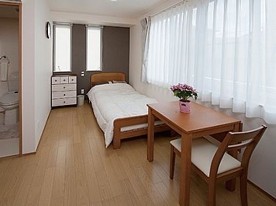 木製の家具とベッドが置かれている施設内の居室。奥の方にタンスがある心地よい場所