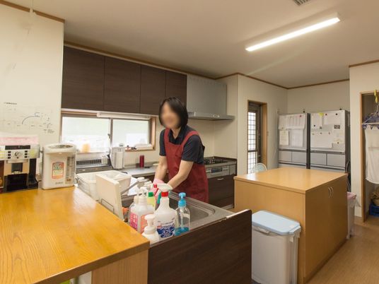 エプロン姿の女性スタッフがキッチンで作業をしている様子。大きな作業台もある。