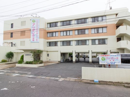 4階建ての白い建物の中央にはベージュのラインが横に入り、屋外階段や駐車場もある。