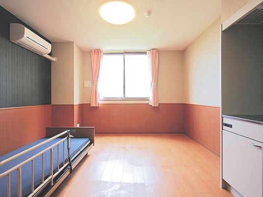 フローリングの部屋にはエアコンやベッド、キッチンがあり、カーテン付きの大きな窓もある。