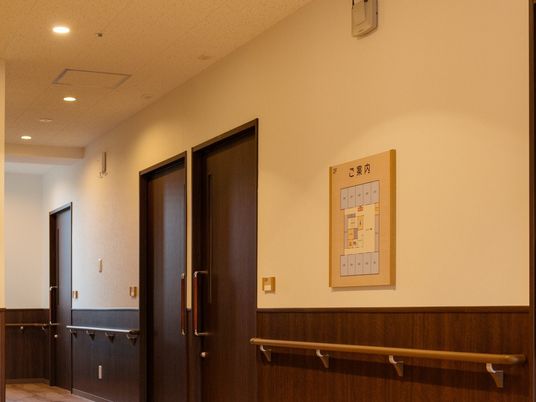 濃い色合いのフローリング、ドアが見えている施設内の写真。手すりがある廊下