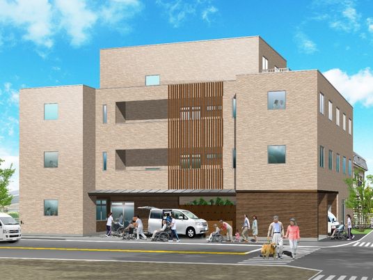 青空の下に建つ大きめの建物の様子。駐車場や遊歩道がある様子が分かる