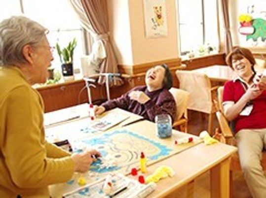 スタッフと工作をしながら笑顔で会話している高齢者。施設内のレクリエーションの様子