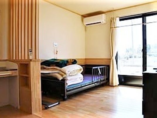 介護用ベッドが置かれたフローリングの居室には大きな窓やエアコン、洗面所が付いている。