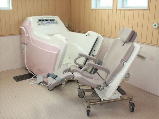 白とピンクの機械浴が置かれたタイル張りの浴室。座ったまま入浴可能な設備で、介護度の高い人も無理なく入浴することができる。