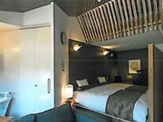 ベッドが２台並べられた部屋。寝具がセットされ、天井が高く、間接照明がうまく使われている。