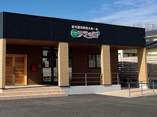 平屋建ての建物は日当たりのいい場所に建っている。外壁にはホーム名が書かれ、駐車場がある。