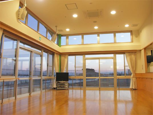 施設内の広めのホールの写真。２面が窓になっていて明るく火が差し込む空間