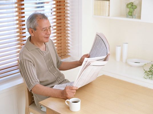自分の部屋で新聞を読んでいる高齢者。コーヒーを手元において真剣な様子で見ている。自分の部屋でのんびりしている様子。