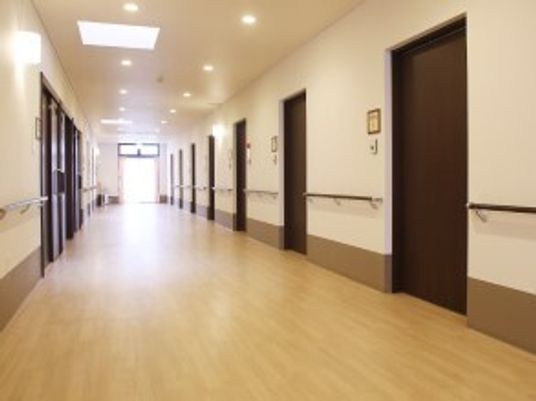 まっすぐな廊下の両サイドには手すりが設置され、居室のドアも並んでいた。突き当りの大きな窓からは陽の光が差し込んでいる。