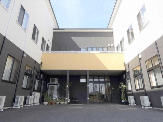 モノトーンカラーの2階建ての建物はコの字型。玄関先には屋根があり、植物が植えられたプランタープが置かれている。