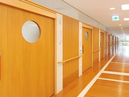 フローリング仕様の廊下と個室の入り口の様子。丸い窓がついた引き戸のドア