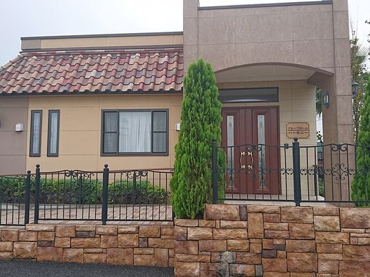 南フランス風のカラフルな瓦屋根が付いた平屋建ての建物の周りには草木が植えられ、玄関には屋根もある。