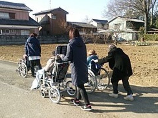 ホーム周辺の散歩を楽しむ車いすの高齢者立ちに付き添うスタッフたち。車いすを押している高齢者もいる。
