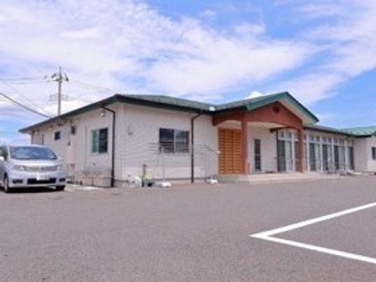 広い敷地内にはグリーンの屋根が付いている平屋建ての建物があり、グレーの車が止まっている。