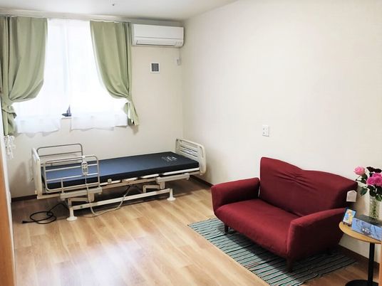 赤いソファと介護用ベッド、テーブルが並べられている日当たりの良い部屋
