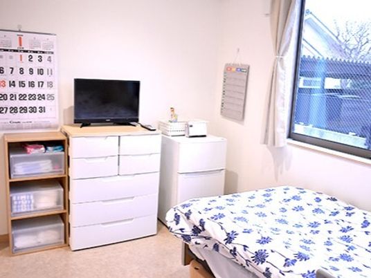 寝具付きのベッドが置かれた部屋にはテレビや冷蔵庫、プラスチックのタンスなどが置かれている。