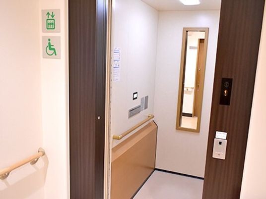 エレベーターの庫内には鏡と手すりがあり、扉の外側にはエレベーターのサインがある。