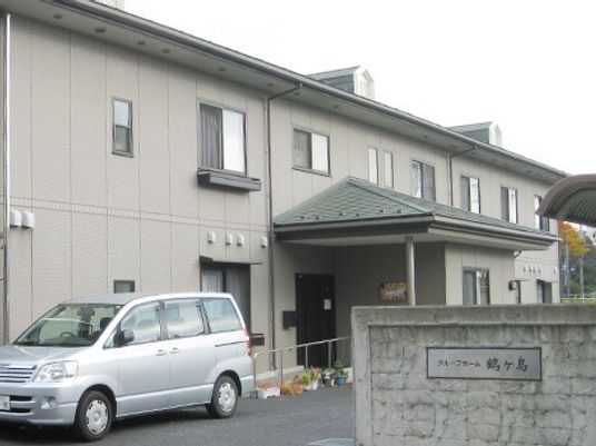 ２階建てのグレーの建物。敷地内には駐車スペースがある。