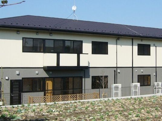 ２階建ての建物。１階はグレーの外壁、２階は白い外壁、屋根は黒く、和風の雰囲気。