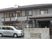 グレーの２階建ての建物。玄関の近くには車が止められている。