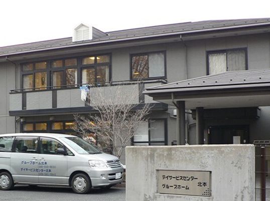 グレーの２階建ての建物。玄関の近くには車が止められている。