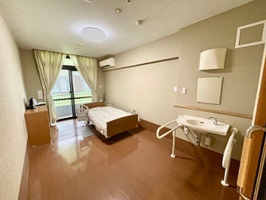 介護ベッドや大きな窓があるフローリングの部屋には車いす対応の洗面所屋エアコンがある。