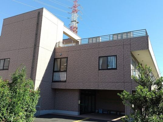 レンガ調の外壁の２階建ての建物は日当たり良好で、周りには草木も植えられている。