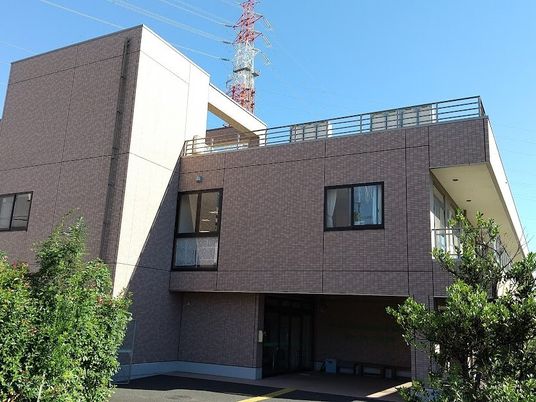 レンガ調の外壁の２階建ての建物は日当たり良好で、周りには草木も植えられている。