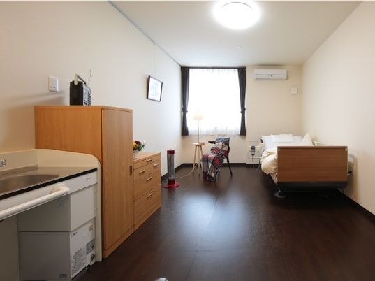 ドレッサータイプの洗面台やたんす、ベッドなど日用品が整った施設内の居室の様子