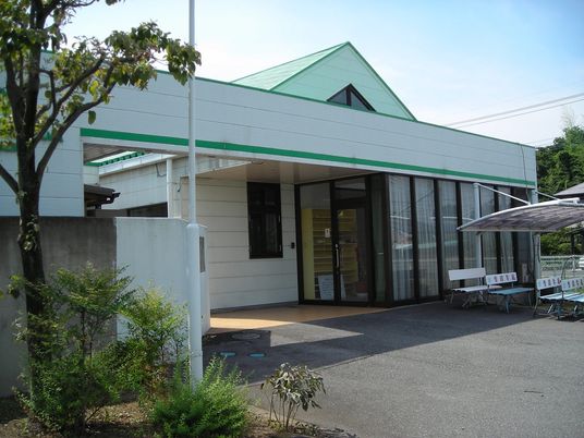 白い外壁の平屋建ての建物にはライトグリーンの屋根が付いていて、屋外にはベンチが並んでいる。