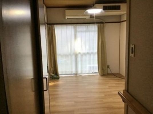 エアコンが付いたフローリングの部屋には家具はなく、レースカーテンとカーテンが付いた大きな窓がある。