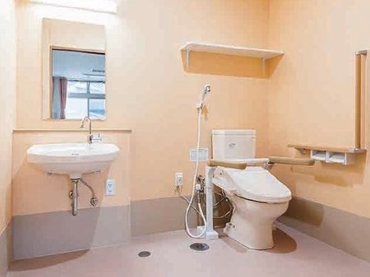 手すりと洗面台がついた広めのスペースのトイレ。サービス付き住宅内に用意された設備