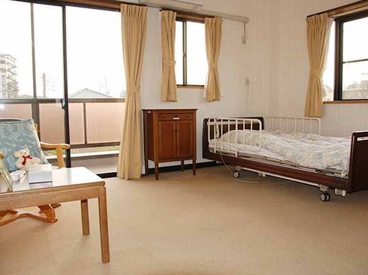 寝具付きのベッドやテーブルセット、収納家具が置かれた広い部屋にはたくさんのカーテン付きの窓がある。