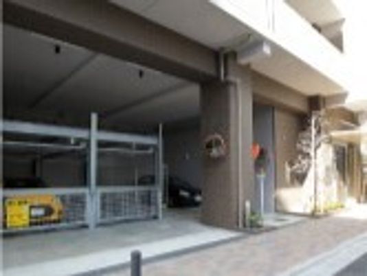 大きな建物の1階部分には駐車場があり、複数台の車が止まっている。その前にはレンガが敷かれたアプローチがある。