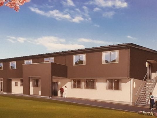 2階建ての建物は白とブラウンで屋外階段が付き、玄関には屋根があり、横に長いデザイン。