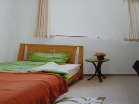 寝具付きのベッドが置かれた部屋には小さなテーブルが置かれ、カーテンが付いた大きな窓がある。