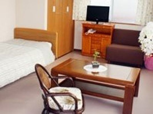 木製のテーブルやいす、テレビ、タンスなどが置いてある施設内の居室の様子