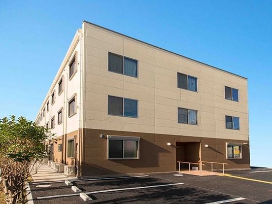 ツートンカラーの建物の外観写真。手前に広めの駐車場があるスペース