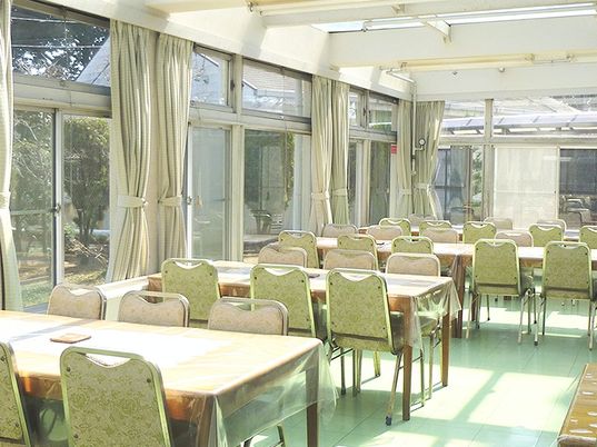 椅子とテーブルが並ぶテラスのような明るい食堂。6人掛けのテーブルが並ぶ空間