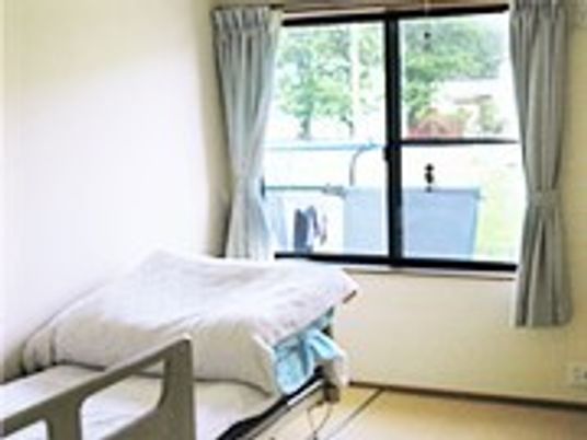 窓際にベッドが置いてある小さな部屋。カーテンがかかった窓から景色が見えている様子